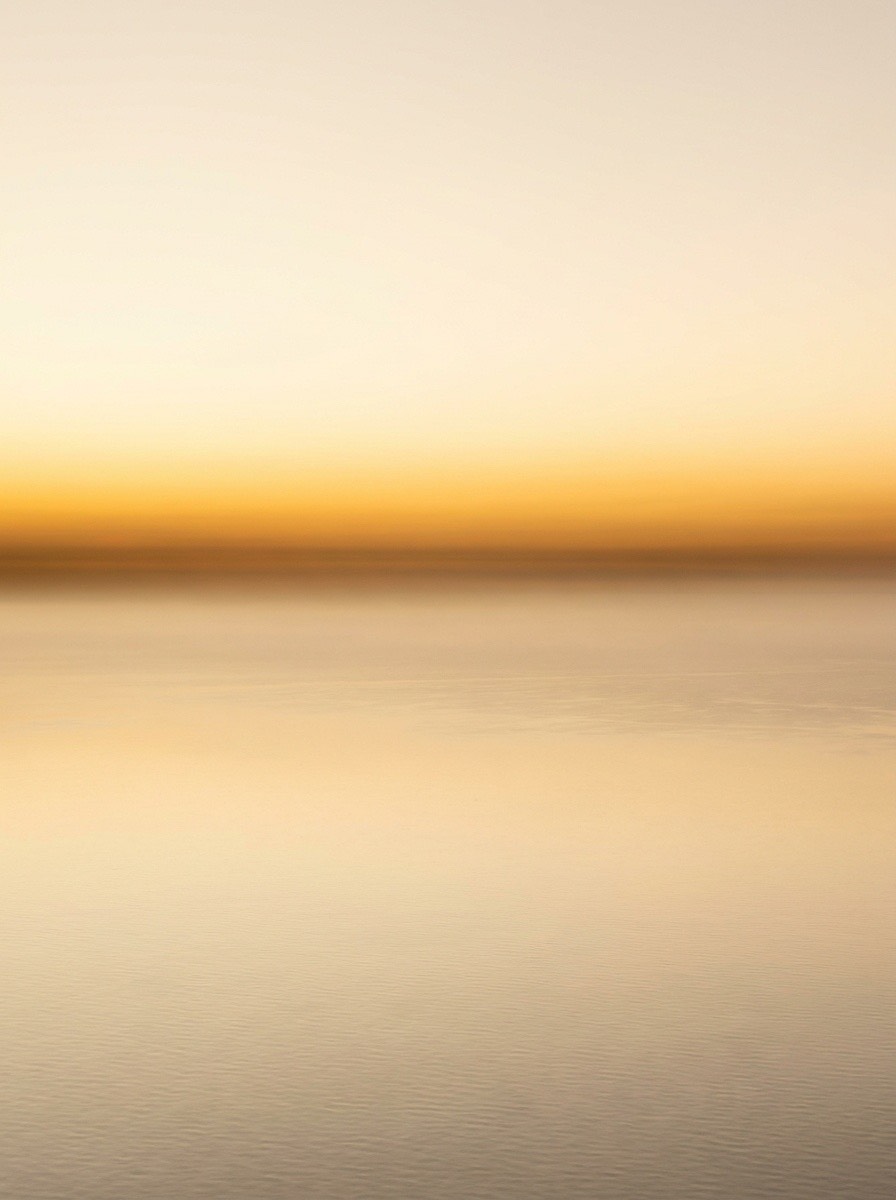 Lever de soleil sur une étendue d'eau calme, bande orangée à l'horizon.